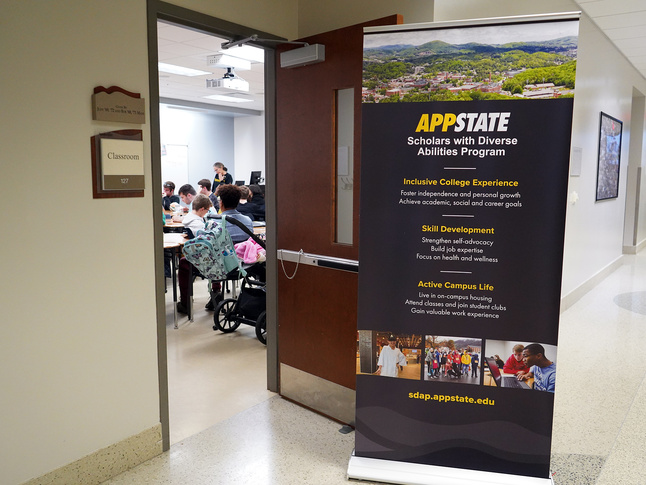 APPSTATE Scholars with Diverse Abilities Program banner in hallway; open classroom with students visible; sdap.appstate.edu